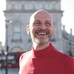 Portrait of a man walking in the street and laughing a lot - Businessman standing in the middle of Piccadilly Circus, London - Bald man wearing a red turtleneck